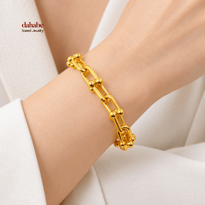 21K yellow gold ball-terminal paperclip bracelet worn on an adult wrist; AI-generated try-on simulation.
