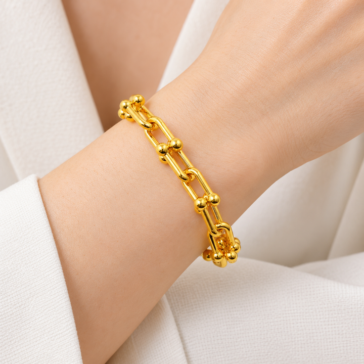 21K yellow gold ball-terminal paperclip bracelet worn on an adult wrist; AI-generated try-on simulation.