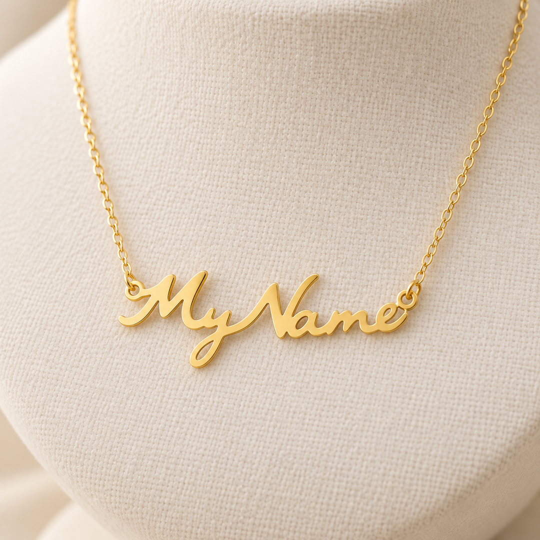 A gold script name necklace reading 'My Name' displayed on a cream fabric jewelry bust.